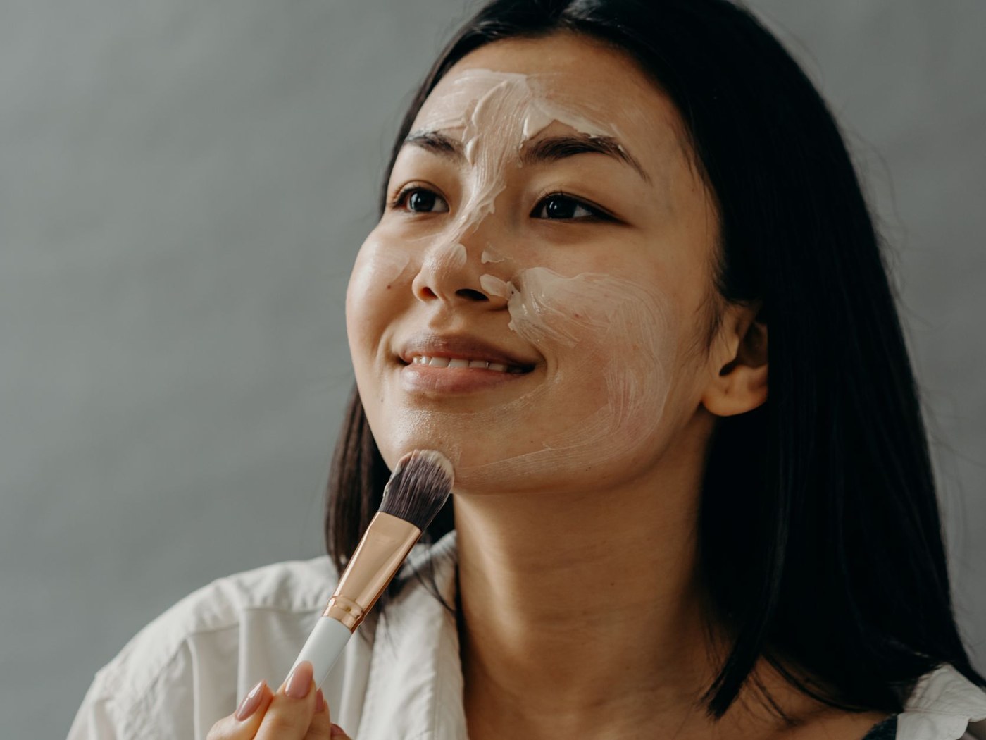 Person applying a powder sunscreen brush across forehead and cheeks over light makeup